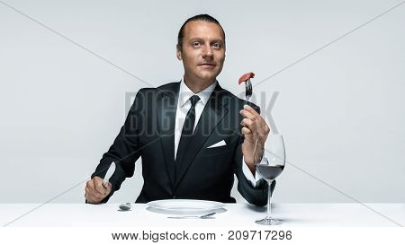 Portrait of a young man in image of maniak with knife, fork and and a piece of raw meat on a plate. Man in suit. The image in the style of Halloween