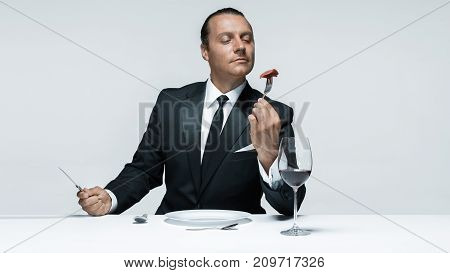 Portrait of a young man in image of maniak with knife, fork and and a piece of raw meat on a plate. Man in suit. The image in the style of Halloween