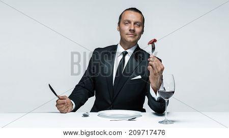 Portrait of a young man in image of maniak with knife, fork and and a piece of raw meat on a plate. Man in suit. The image in the style of Halloween