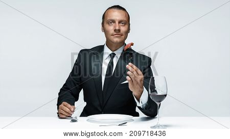 Portrait of a young man in image of maniak with knife, fork and and a piece of raw meat on a plate. Man in suit. The image in the style of Halloween