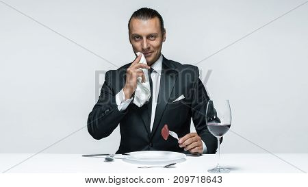Portrait of a young man in image of maniak with knife, fork and and a piece of raw meat on a plate. Man in suit. The image in the style of Halloween