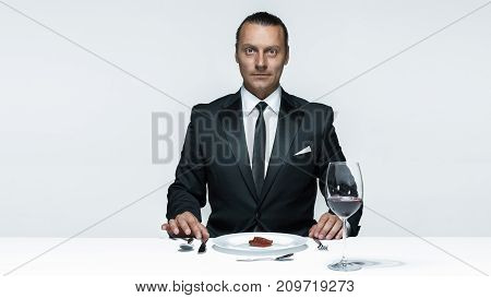 Portrait of a young man in image of maniak with knife, fork and and a piece of raw meat on a plate. Man in suit. The image in the style of Halloween