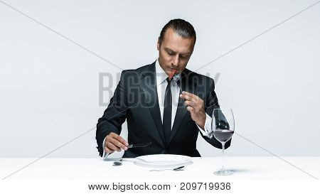 Portrait of a young man in image of maniak with knife, fork and and a piece of raw meat on a plate. Man in suit. The image in the style of Halloween
