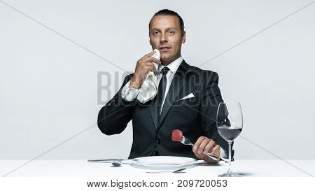 Portrait of a young man in image of maniak with knife, fork and and a piece of raw meat on a plate. Man in suit. The image in the style of Halloween