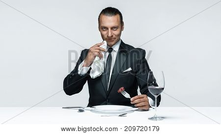 Portrait of a young man in image of maniak with knife, fork and and a piece of raw meat on a plate. Man in suit. The image in the style of Halloween