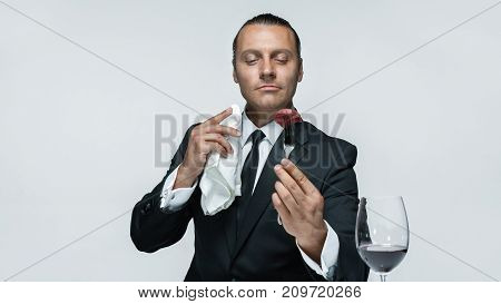 Portrait of a young man in image of maniak with knife, fork and and a piece of raw meat on a plate. Man in suit. The image in the style of Halloween