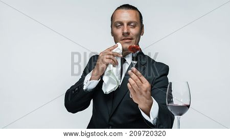 Portrait of a young man in image of maniak with knife, fork and and a piece of raw meat on a plate. Man in suit. The image in the style of Halloween