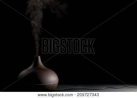 Electric aromatherapy device. Electronic diffuser gadget in use against black background. Steam and essential oil vapour.