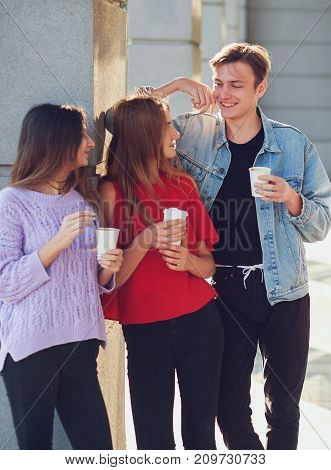Students enjoying cup of coffee to go on street. Young people communicating outdoor at morning with cup of energy drink