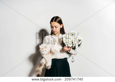 a young beautiful girl holds a big white bouquet of flowers and a white cat in her hands, and she does not like it because she has an allergy