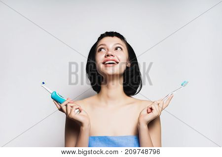 beautiful smiling girl with short black hair chooses which brush to brush your teeth: electronic or ordinary