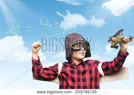 Boy in aviator cap holding toy airplane against blue sky