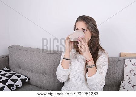Beautiful young woman drinking coffee and relaxed on couch. Indoors.