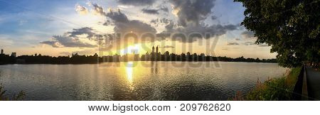 Sunset and silhouette buildings reflects on water at Jacqueline Kennedy Onassis reservoir in panorama