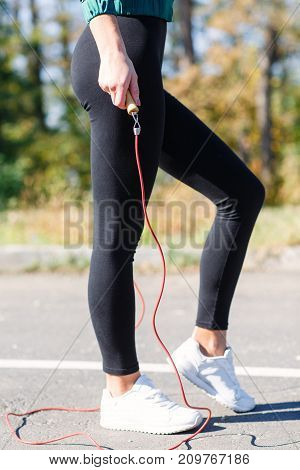 Caucasian young girl doing exercises with jumping rope. White sneakers, black leggings and sexy legs