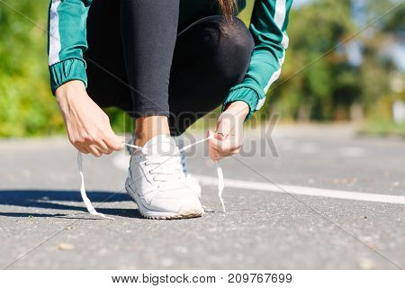 Horisontal photo young athletic girl ties up shoelaces on sneakers