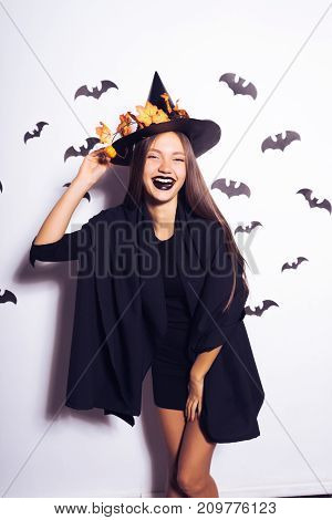 a young sexy gothic girl dressed in a witch for Halloween, in a big black hat adorned with yellow leaves, laughs