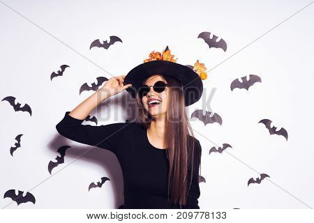 young sexy gothic girl dressed in a witch for Halloween, standing in sunglasses and a big black hat