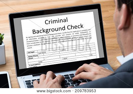 Man Filling Criminal Background Check Application Form On Laptop In Office