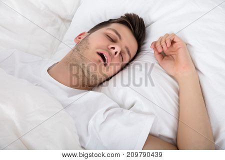 View Of Tired Young Man Snoring While Deep Sleeping In Bed
