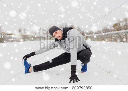 fitness, sport, people, exercising and healthy lifestyle concept - young man stretching leg and warmig up on snow covered winter bridge