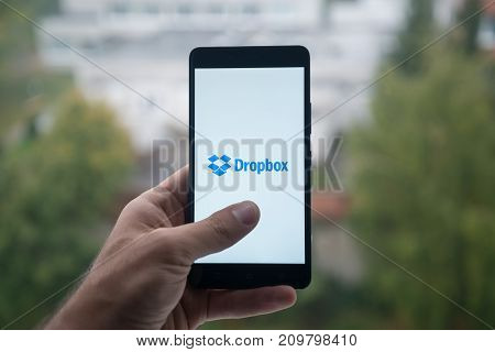 London, United Kingdom, october 3, 2017: Man holding smartphone with Dropbox logo with the finger on the screen