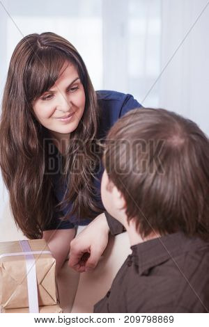 Portrait of Caucasian Brunette Wife Giving a Present to Her Husband Indoors.Vertical Image Composition