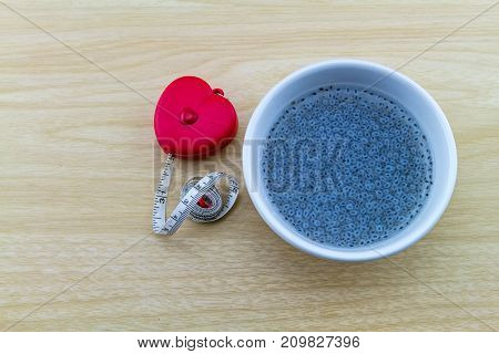 Sweet basil in white cup and red measuring tape shape heart on wooden background.Indicate for slim and good health.