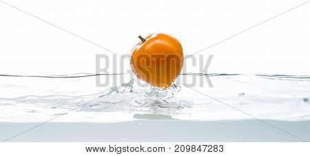 Whole, yellow and ripe tomato falls into the water. Water splashes. Isolated picture on white background
