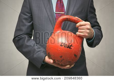 Debt. Debentures. Business man holding in his hands kettlebell with DEBT inscription isolated on grey background.