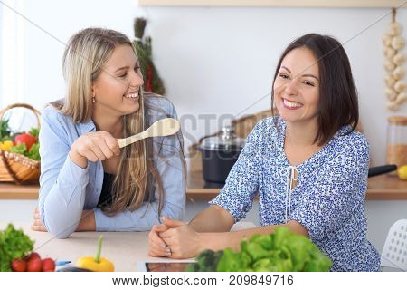 Two young happy women making online shopping for making menu by tablet computer. Friends cooking in the kitchen.