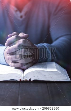 Mid section of man with bible praying at wooden desk