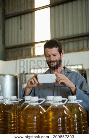 Smiling working taking a photo of olive oil bottles in factory