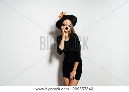 young sexy gothic girl in the image of a witch in halloween, in a big black hat dreamily looks up