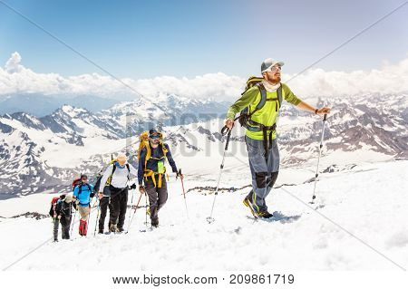 A group of mountaineers rises to the top of a snow-capped caucasian mountain against the backdrop of the rocky peaks of the mountains covered with snow.