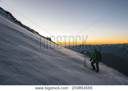 the mountaineer professionally equipped at dawn of the sun walks on the slope in the early morning and the snow drifts over the snow above the snow. The concept of travel and conquest of steep peaks