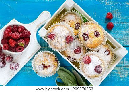 Curd cakes (muffins) with raspberries decorated with powdered sugar. Serve in a white wooden box. Fresh raspberries in a ceramic bowl. Top view.