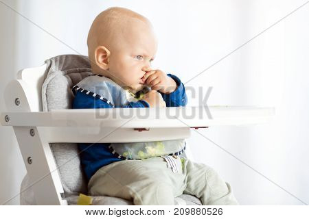 Baby boy eating bread and cucumber with BLW method baby led weaning. Serious vegetarian kid eating lunch. Child eat himself self-feeding.