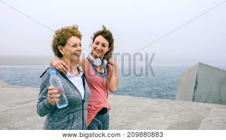 Senior woman and young woman walking outdoors by sea pier