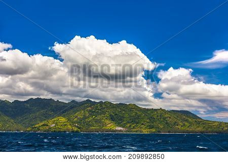 Farmland and rice fields on the sunny slopes of the island beautiful clouds over it view from the Bali sea space for text. Lombok island, Indonesia.