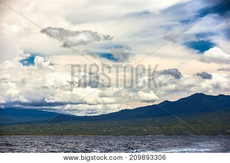 Forest on the mountain slopes of the island beautiful clouds above it view from the Bali sea space for text. Lombok island, Indonesia.