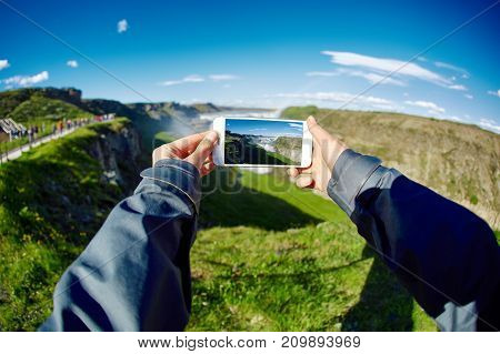 Hands holding a smartphone with a picture of the landscape - famous Gullfoss waterfall in southern Iceland. treking in Iceland. Travel and landscape photography concept
