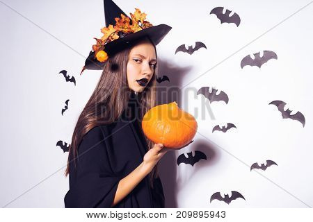 young gothic sexy girl in the image of a witch celebrating halloween, holding a pumpkin
