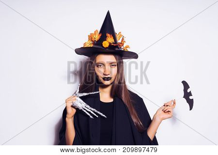 a young gothic sexy girl in the shape of a witch celebrates halloween, in a black big hat decorated with golden maple leaves