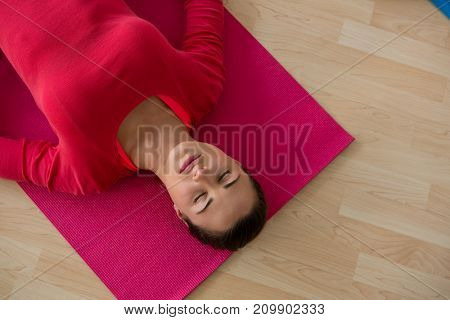 High angle view of young woman exercising while lying on mat in yoga studio