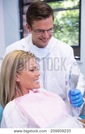 Dentist showing mirror to smiling patient at dental clinic