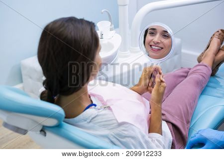 Happy woman looking at mirror while sitting on dentist chair at medical clinic