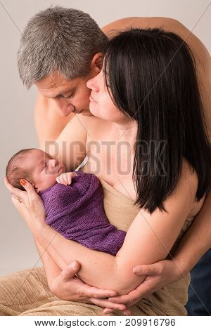 Happy family couple in love on the background. Portrait of happy young family tenderly keeping their sleeping baby on gray background.