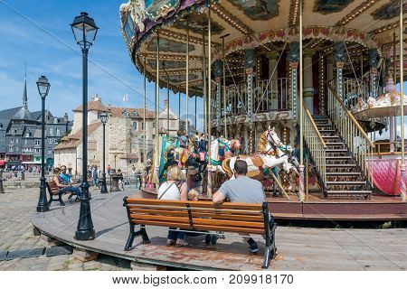 HONFLEUR, FRANCE - AUGUST 24, 2017: Caroussel at the harbor of Honfleur with little girls riding a horse while the parents are waiting at a bench