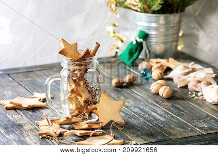 Homemade shortbread star shape sugar cookies different size in glass jar and as garland on old wooden table decorated by Christmas tree and gifts. Christmas mood theme.